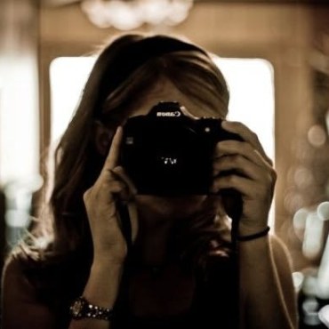 Amanda holding a camera to her eye, backlit