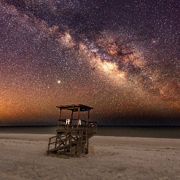 The Milky Way arcing over a lifeguard tower on a dark beach